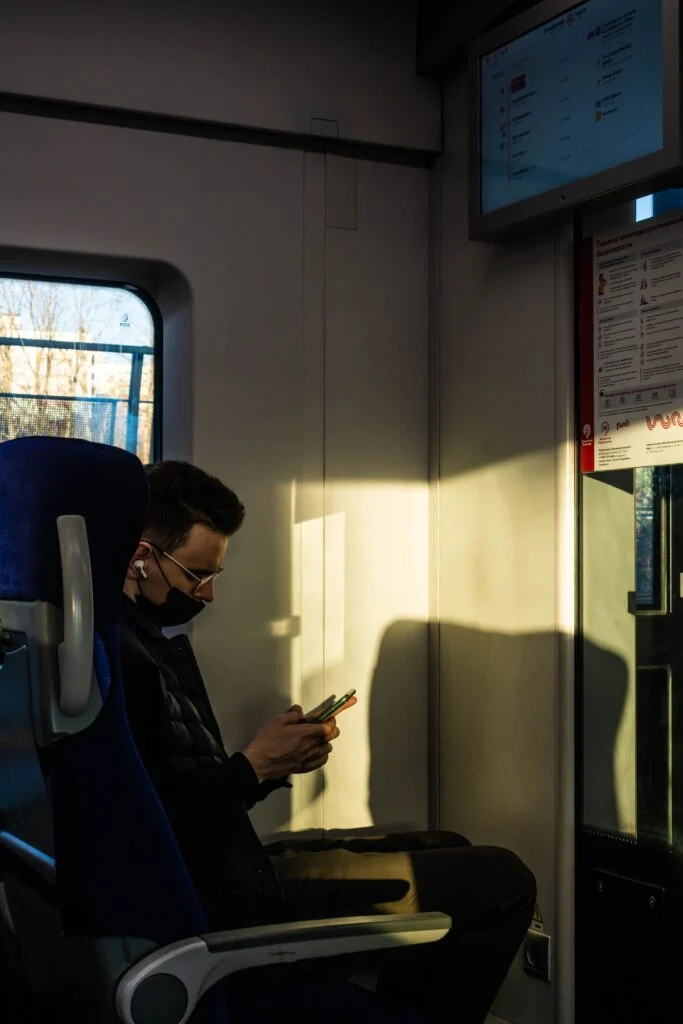 Passenger sitting by a train window playing free browser games on a phone during a long commute, with Mugeri Games open on screen